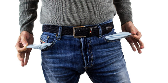 Blick auf die Körpermitte eines Mannes in Jeans.. Er zieht sich beidseitig die leeren Taschen aus der Hose.